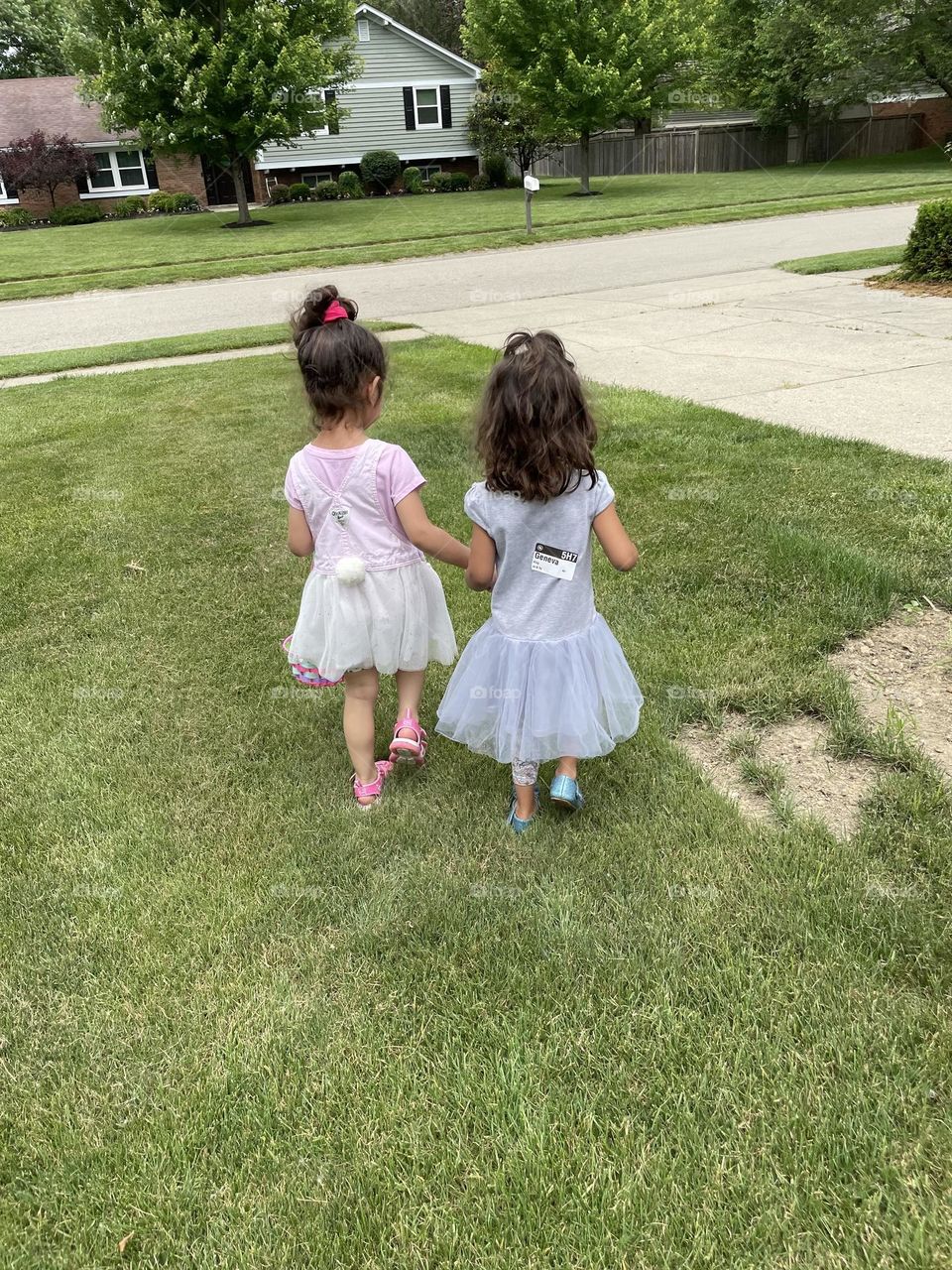 Two little girls walking together holding hands, two toddler friends holding hands, little girls playing together in the summertime 