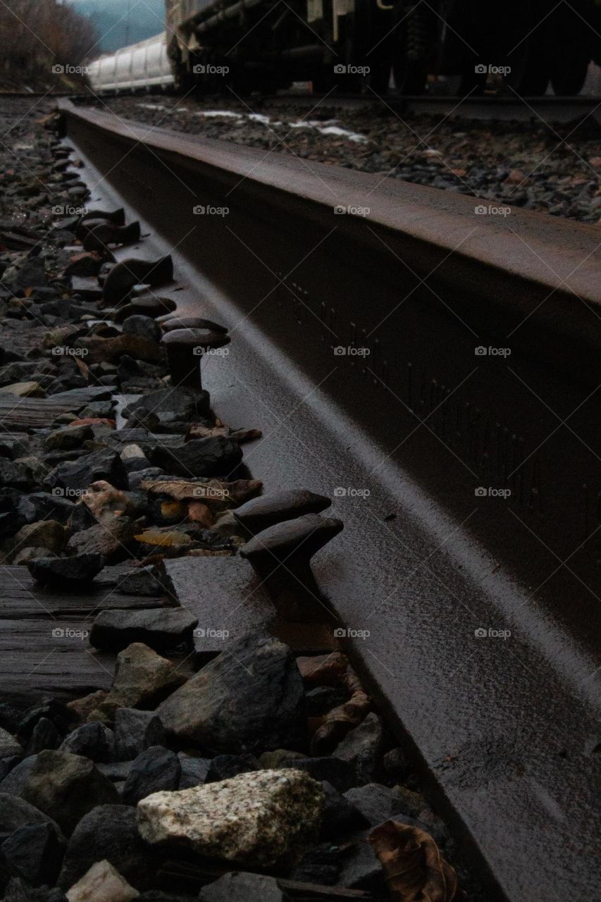 Damp metal railroad tracks surrounded by stones with wooden beams and metal stakes places two by two.