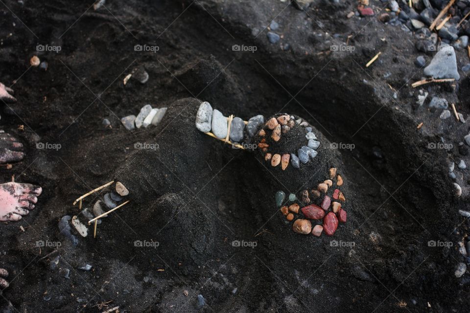 A black sand castle decorated with stones on the beach.