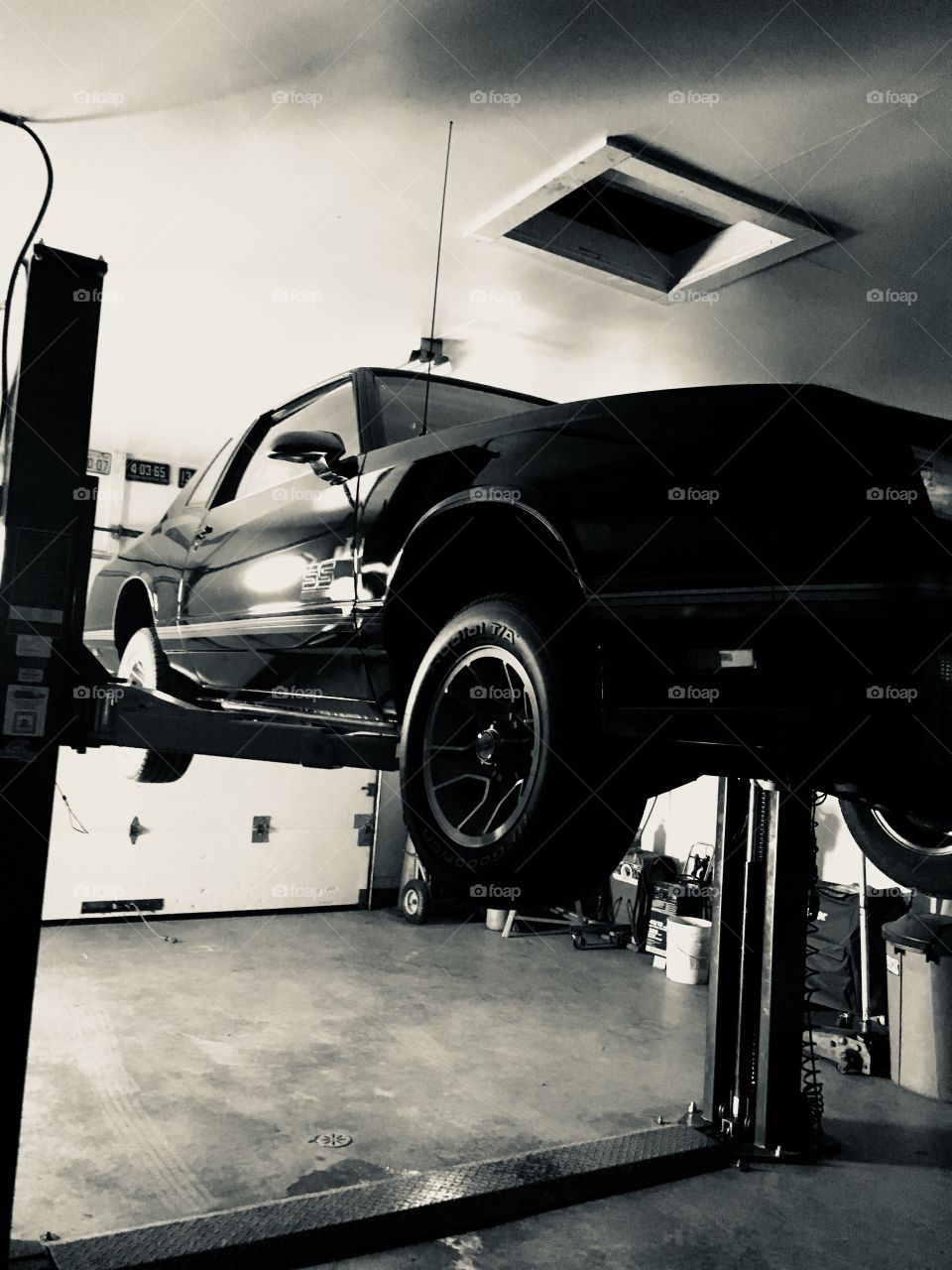 Black 1987 Chevrolet Monte Carlo SS on hoist in a garage. Black and white photo. 