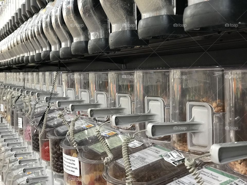 Rows of nuts and dried foods in their containers with self serve scoops in the bulk foods section of the grocery store. 