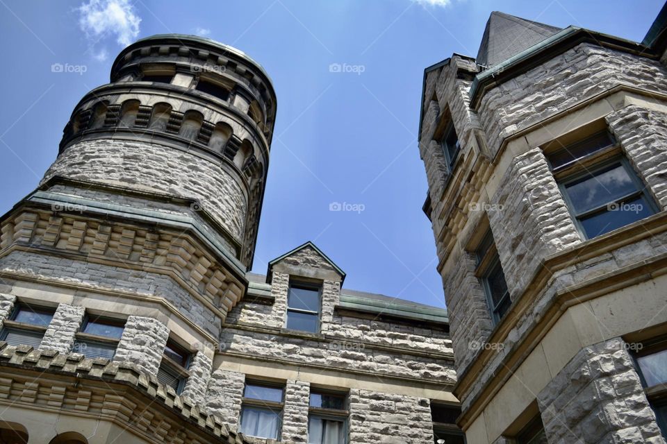 The top of a grey brick building that looks like a castle with turrets and windows against a blue sky