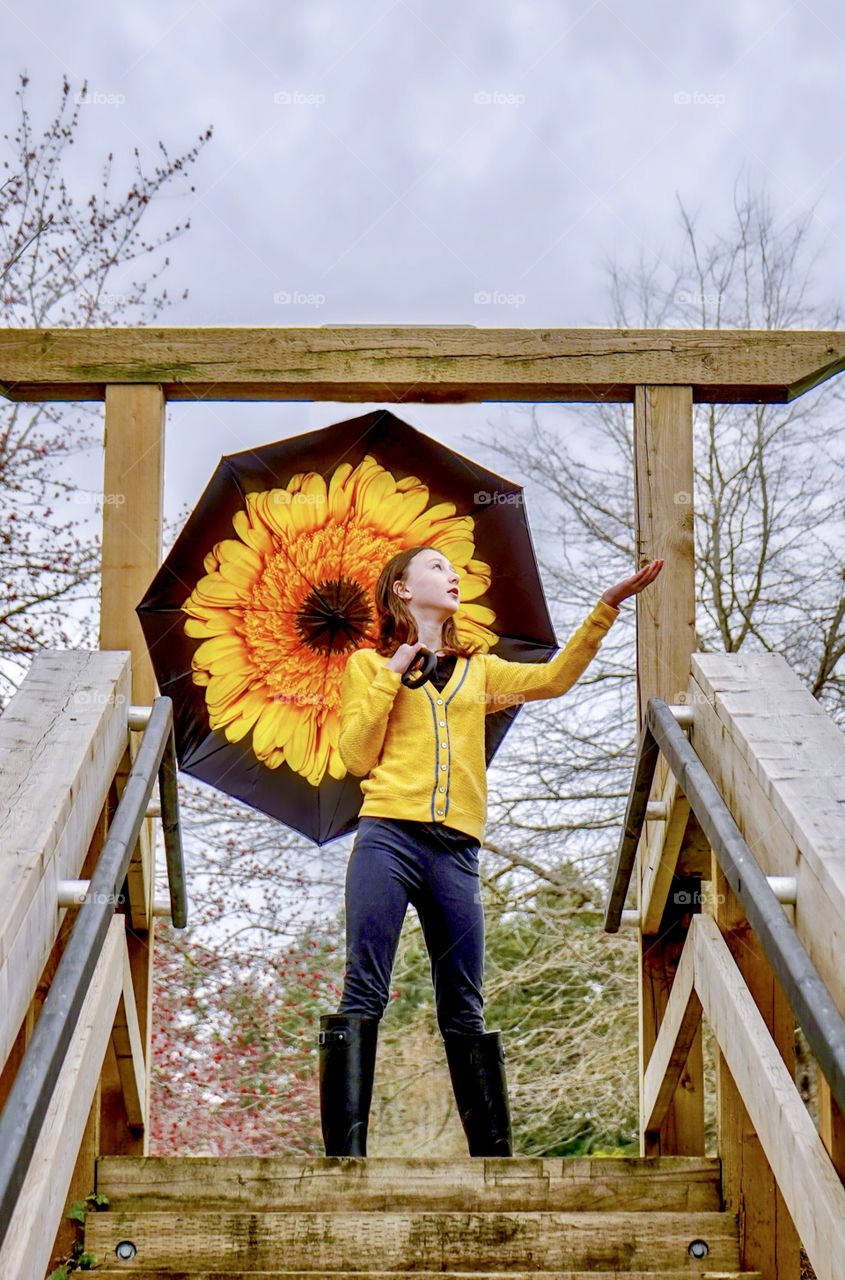 Girl under big flower umbrella checks for rain 