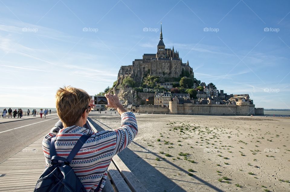 Tourist takes a photo of Mont Saint Michel with her smartphone 