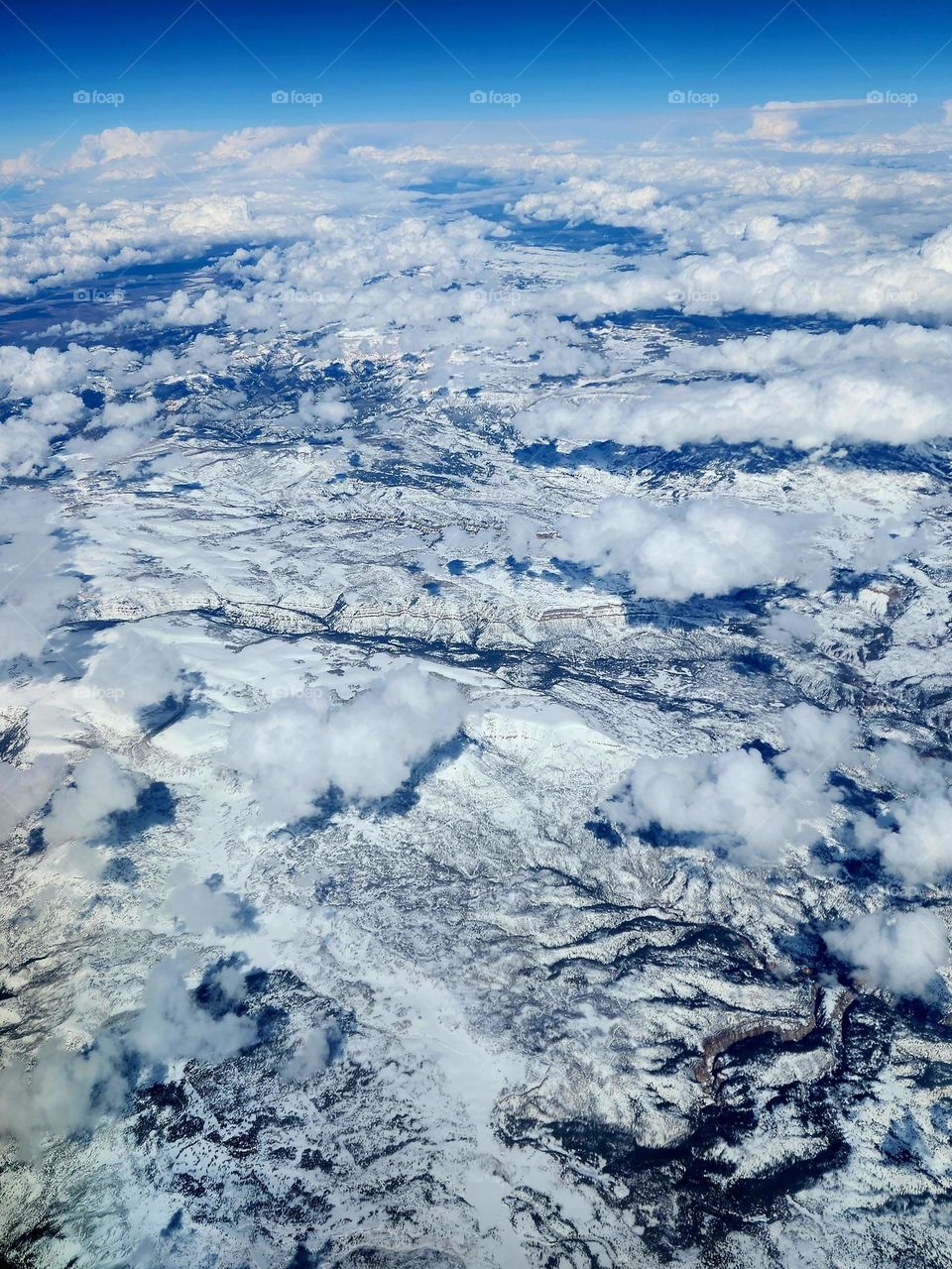 Although it's almost Spring, snow covers a vast mountain range in the southwest US punctuated by cotton-like cumulus clouds