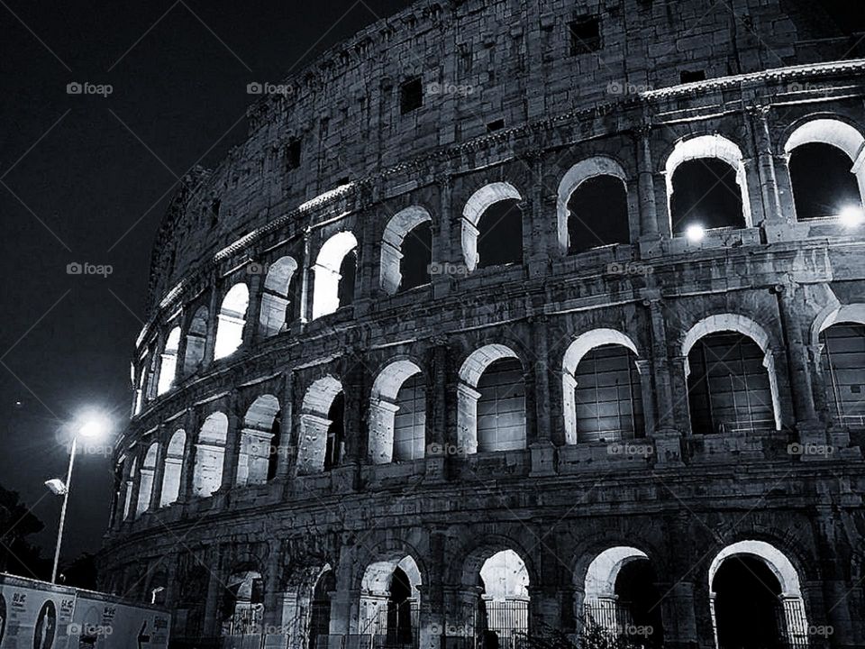 B&W.  Italy.  Rome.  Part of the Colosseum at night.  The Colosseum is illuminated by street lights and interior lighting.  Monument of architecture and history of the country