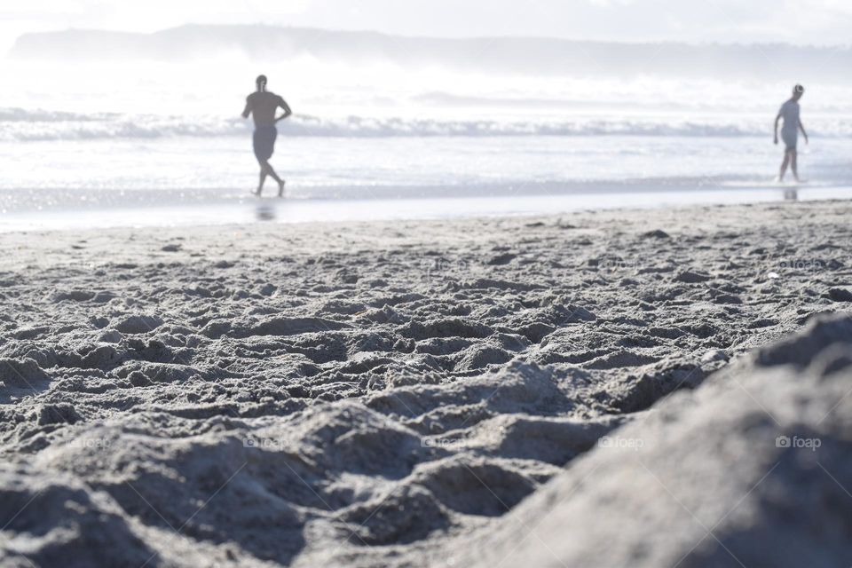 Blurry silhouette of man on beach running into ocean waves with sand in foreground 