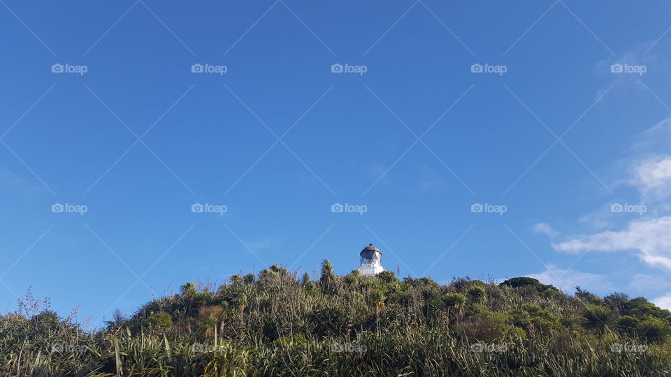 Lighthouse in New Zealand. Top of hill with blue sky above.