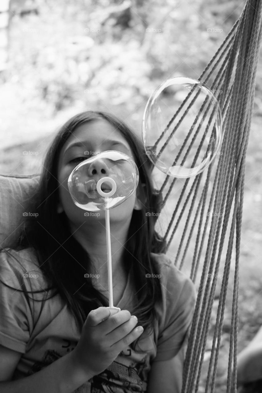 Long hair boy blowing soap bubbles on an hammock 