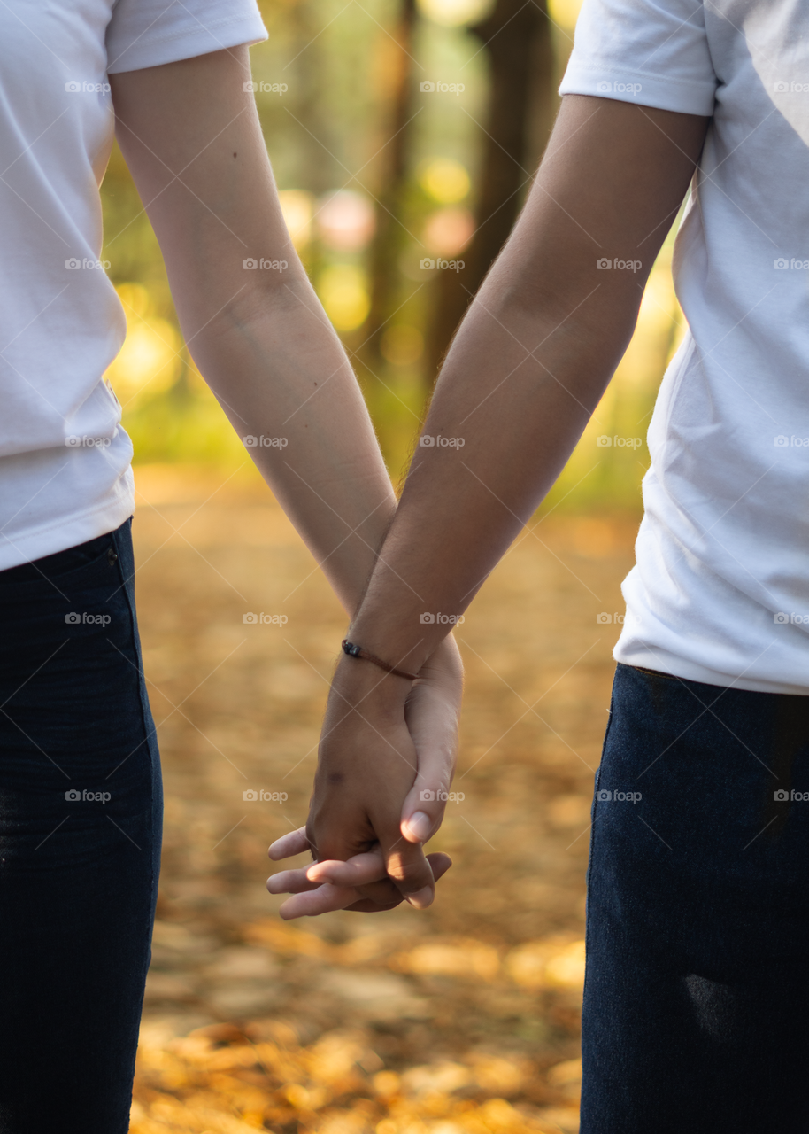 Couples of young people walking in middle of the forest while taking their hands together, in a sunny day.