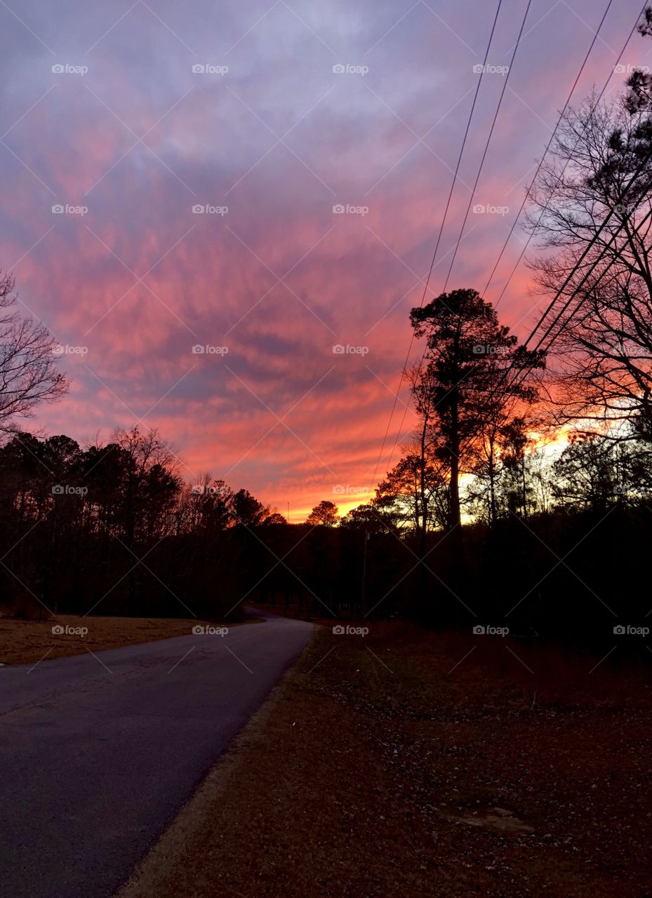 Sun setting behind hillside ridge while illuminating cloud bank as dusk emerges 