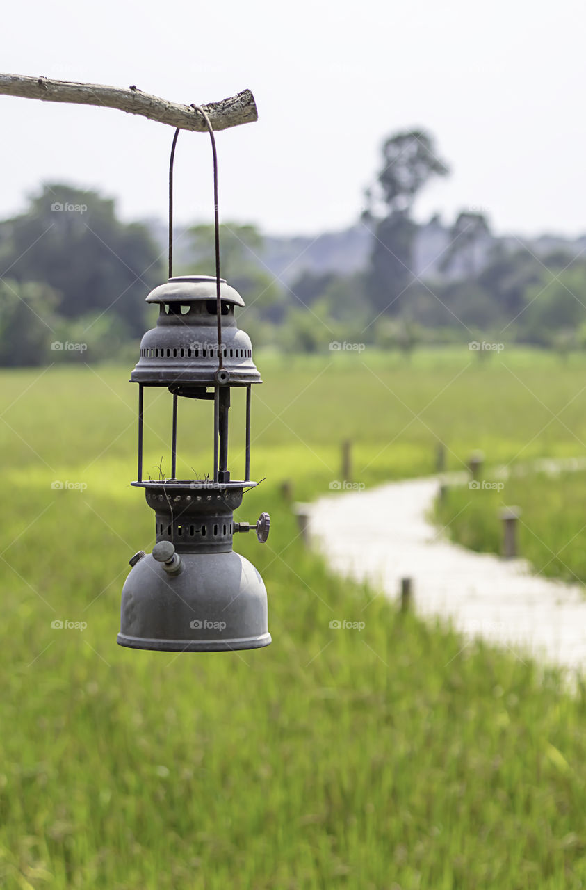 Old lantern hanging on wooden background fields and wooden bridge.