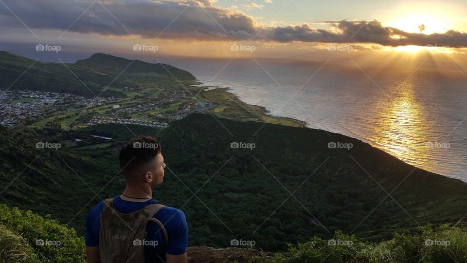 Man standing on mountain peak in front of sea during sunrise