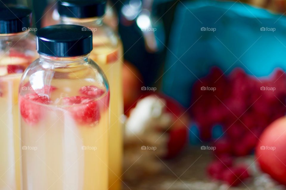 Closeup of kombucha, bottled for a second-ferment and flavored with nectarines and raspberries and slices of ginger root, whole ingredients in the background