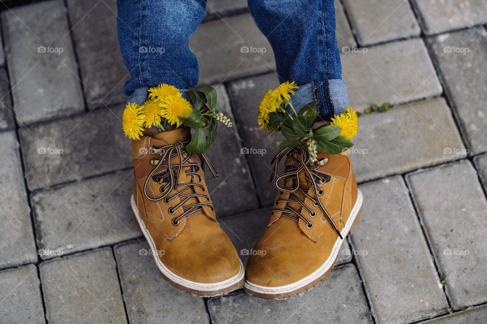 One of the first spring flowers are dandelions. Cute boy shoes with bright yellow flowers inside.  Blue jeans