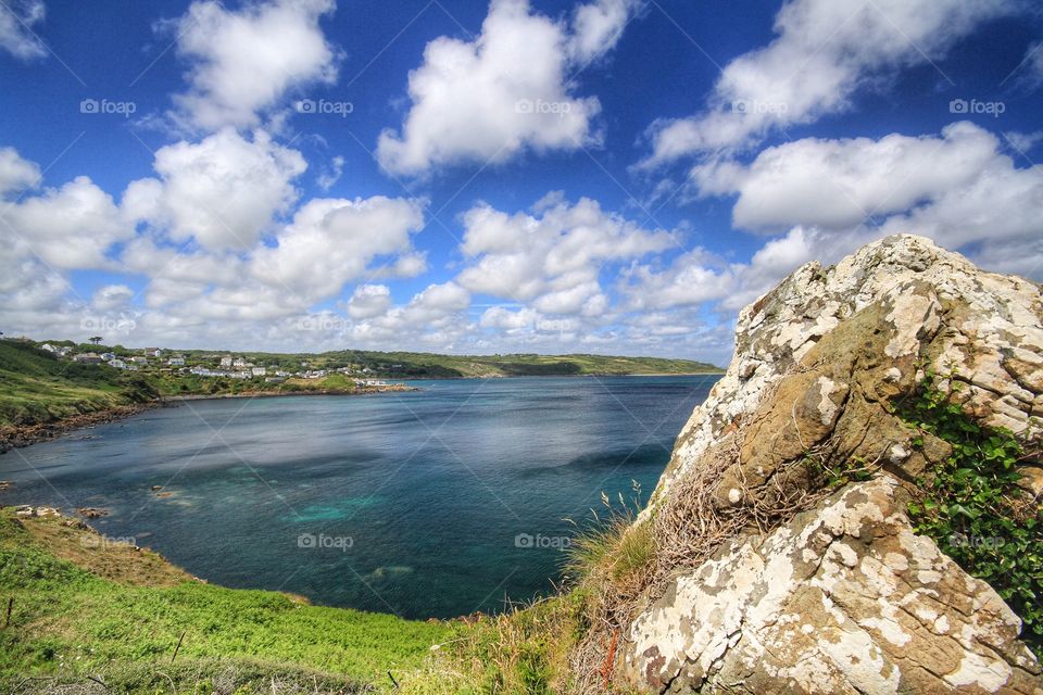 A summer coastal scene in Cornwall with green sea and blue skies. Emerald green ocean and blue sky with fluffy white clouds.