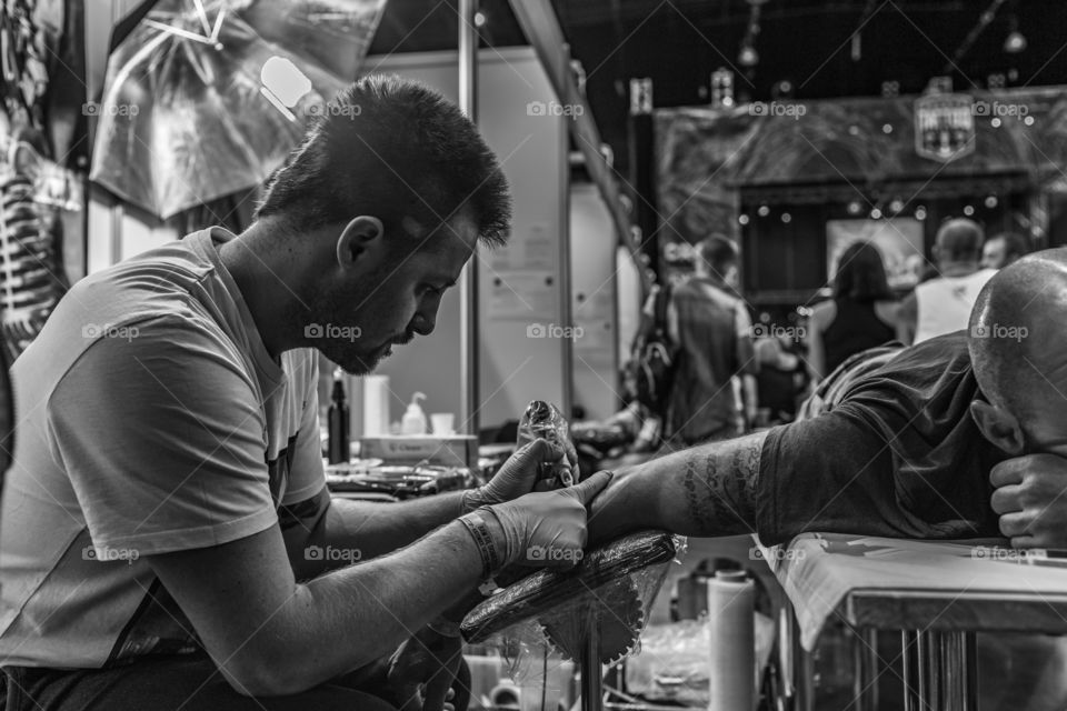 Tattoo artist making tattoo on person's hand