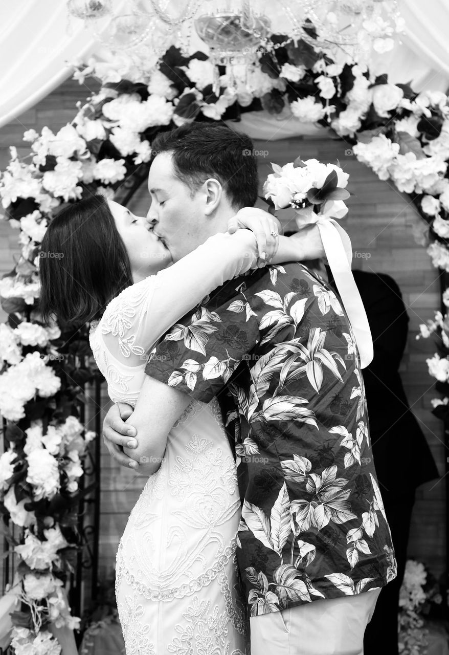 Married couple kissing in front or flower arch b&w