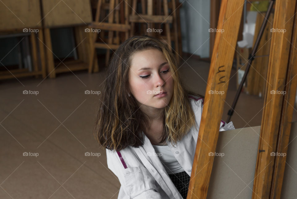 Portrait of young beautiful girl teenager - artist painting behind a wooden canvas