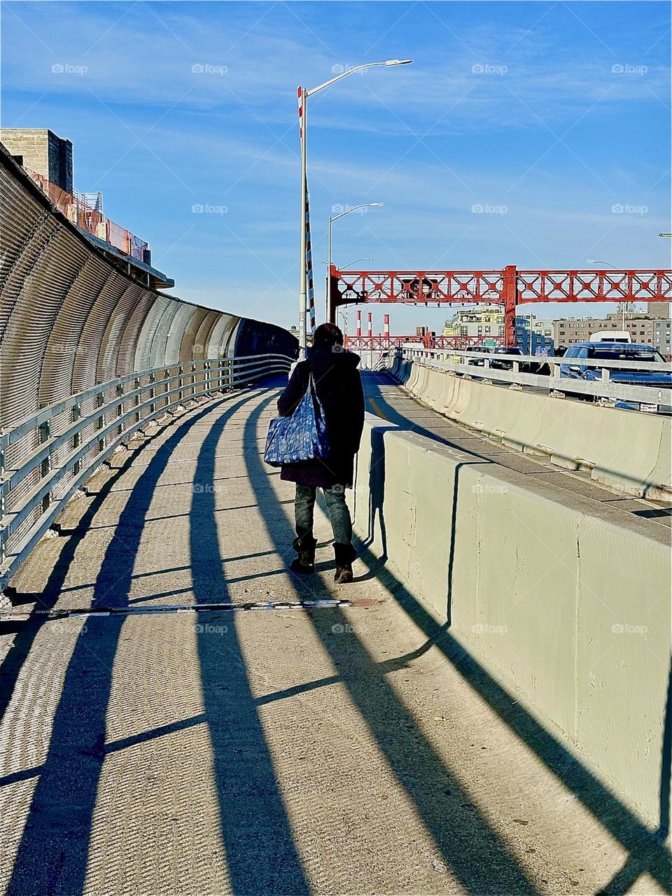 The pedestrian lane of the “Pulaski Bridge” traveled by the lady in black from “Greenpoint”, Brooklyn to LIC, Queens has deeply pronounced shadows etched into it by the late afternoon sun along its curved trajectory. 2023. Hypnotic Productions
