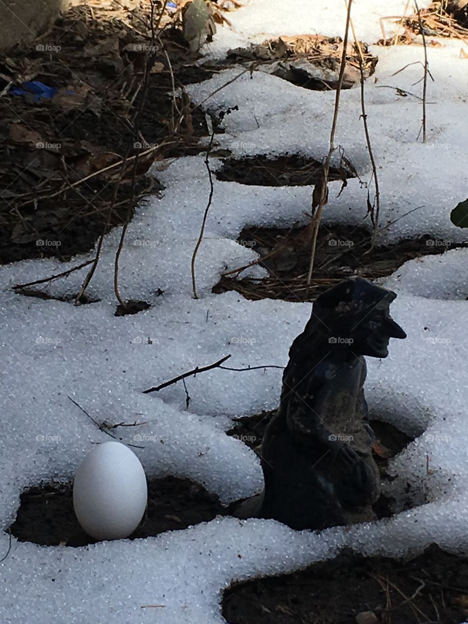 Out with the old, in with the new.  A balanced egg next to a crone figurine in icy snow. 