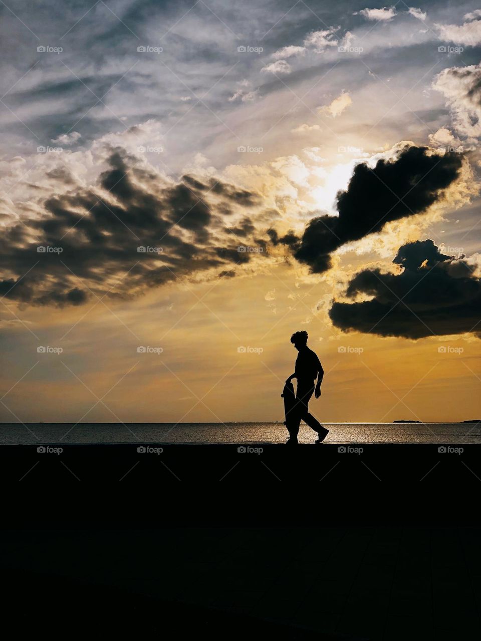 Silhouette of a young man with a skateboard at sunset