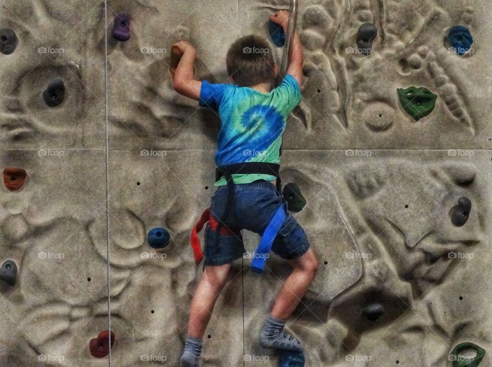 Young Rock Climber. Young Boy Scaling A Rock Wall
