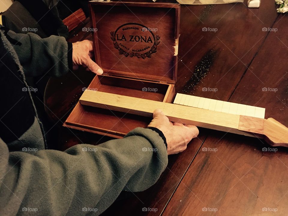 Working man using his hands to put the neck of a guitar he made , into the body of the wooden guitar.
