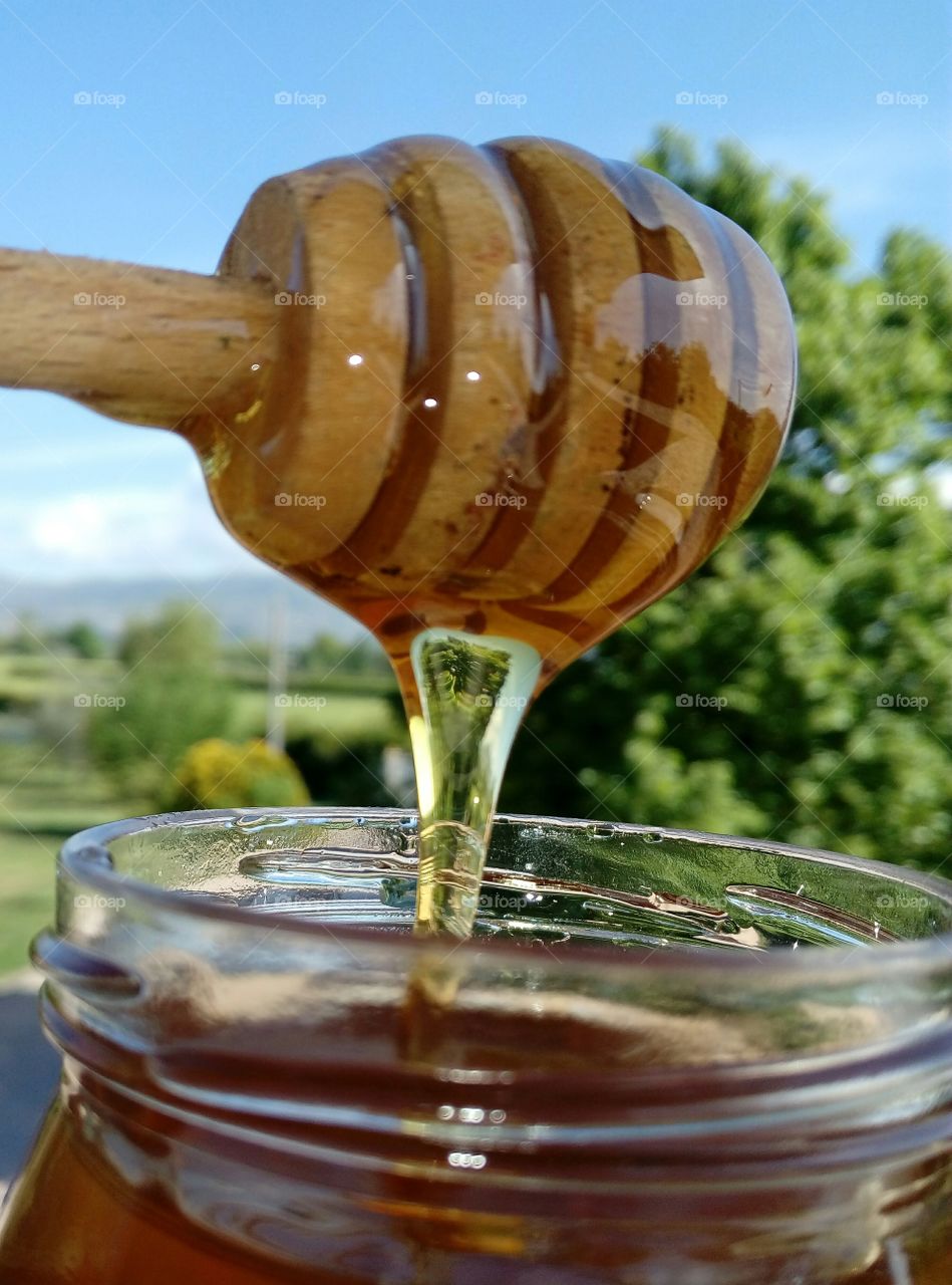 Glass jar of honey with wooden dipper at outdoors