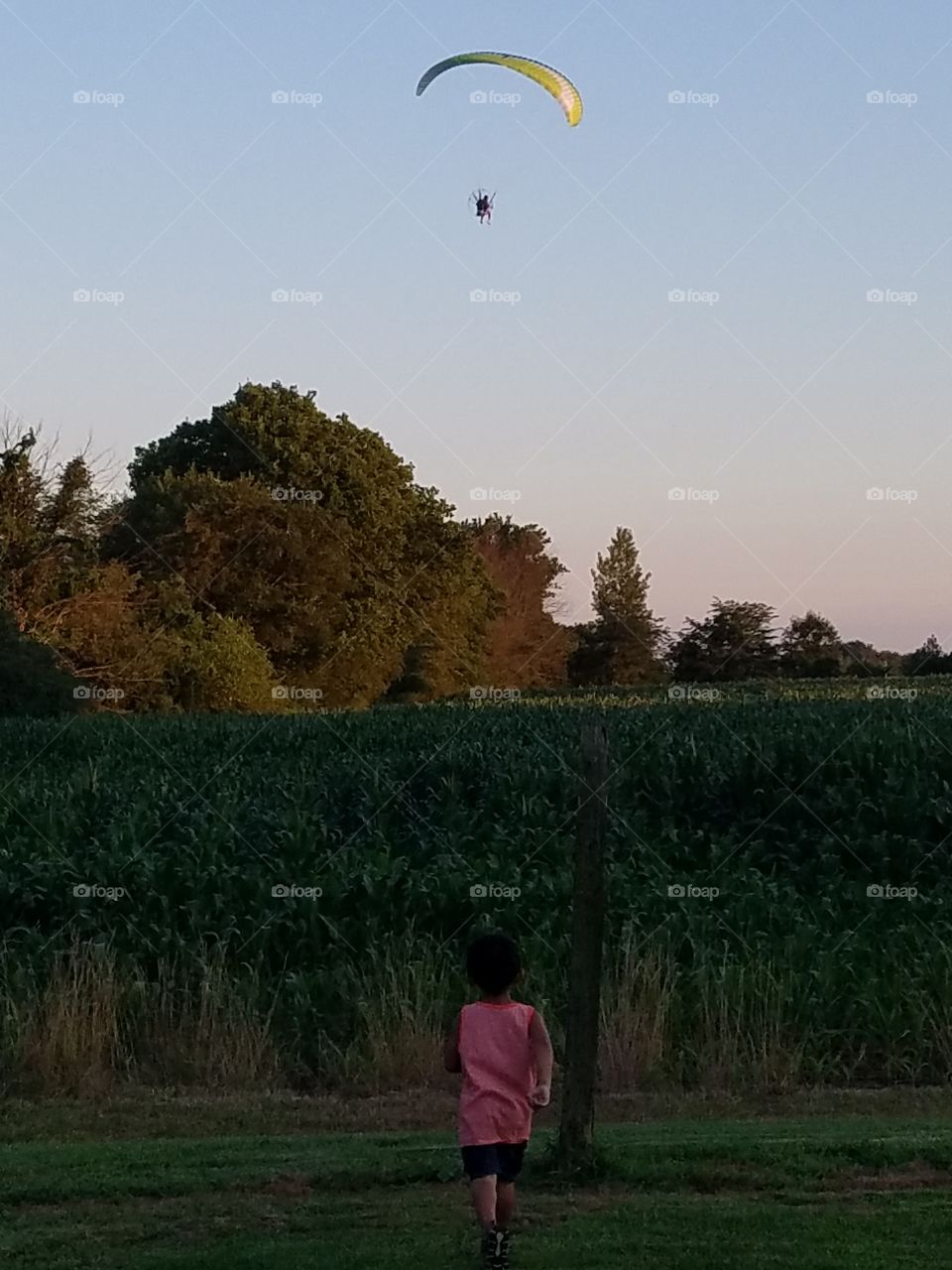 cool picture of kid running to see folks parachute glider in the sky