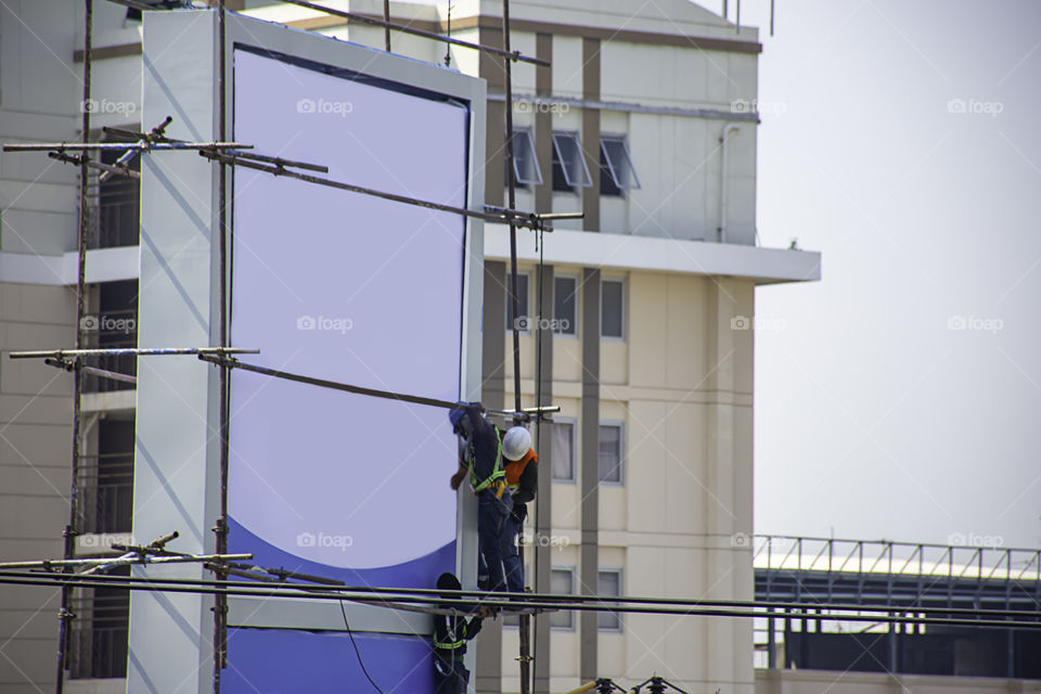 Workers on the scaffold are installing billboards.