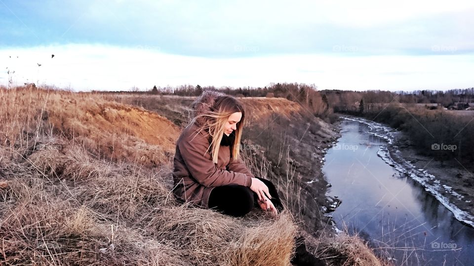 Girl sitting on the edge watching sunset and listening river flow