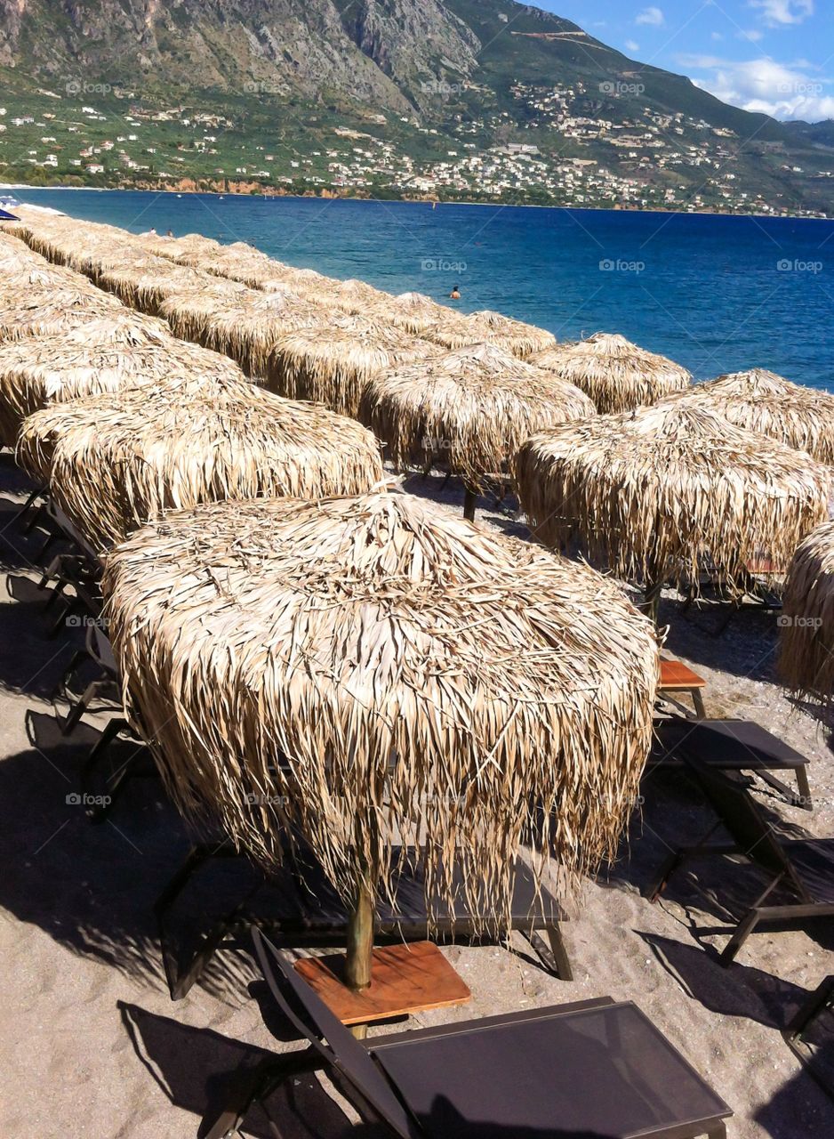 Kalamata city beach. Sun umbrellas from straw on Kalamata beach against mount Taugetos and cloudy sky
