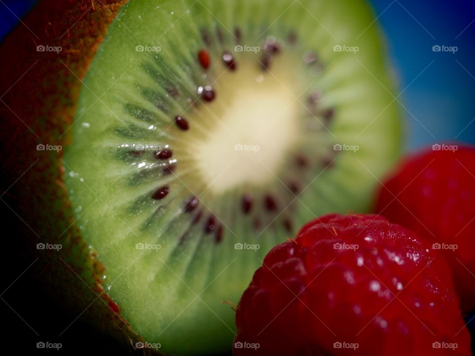 A close up of a kiwi fruit and raspberries