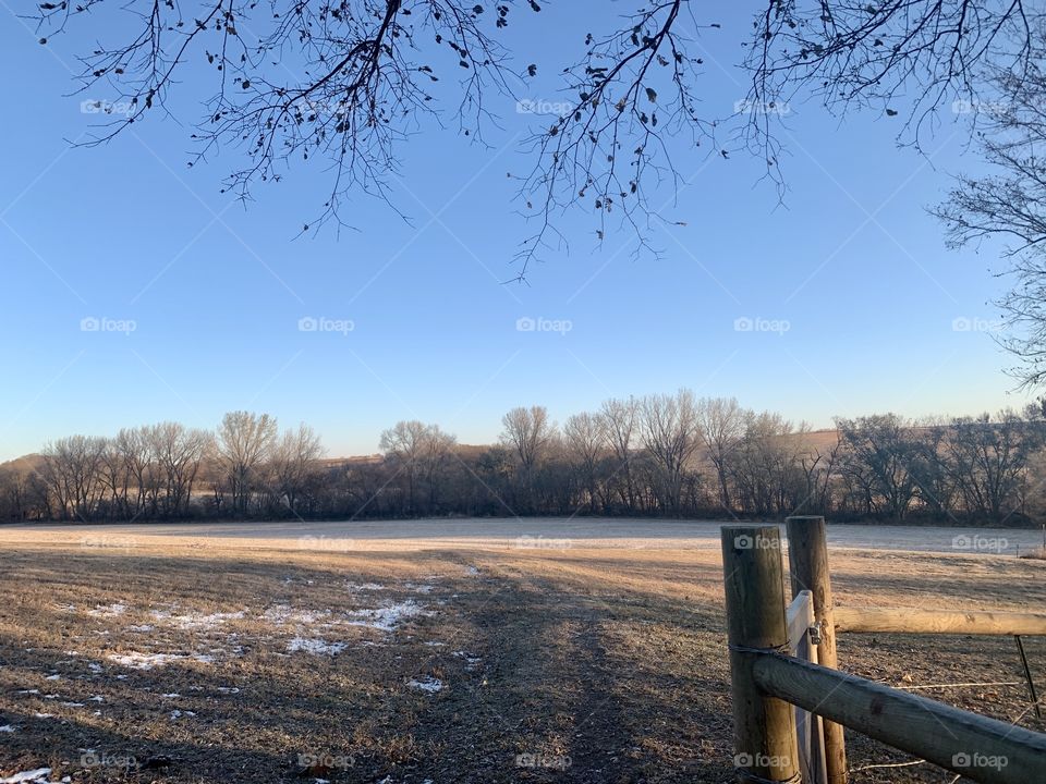View from a wooden gate across an empty farm field to bare trees in distant hills on a beautiful autumn day- landscape