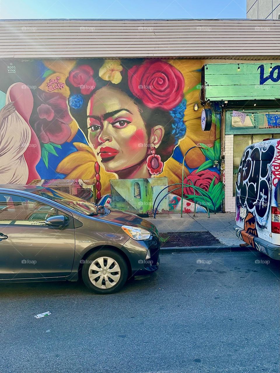 A mulatto Latina with a red nose in her hair is featured on “Jefferson St” off “Broadway” in “Bushwick”, Bklyn as part of an art mural that covers nearly an entire city block next to the club restaurant “La Lupe”. 2024. Hypnotic Productions