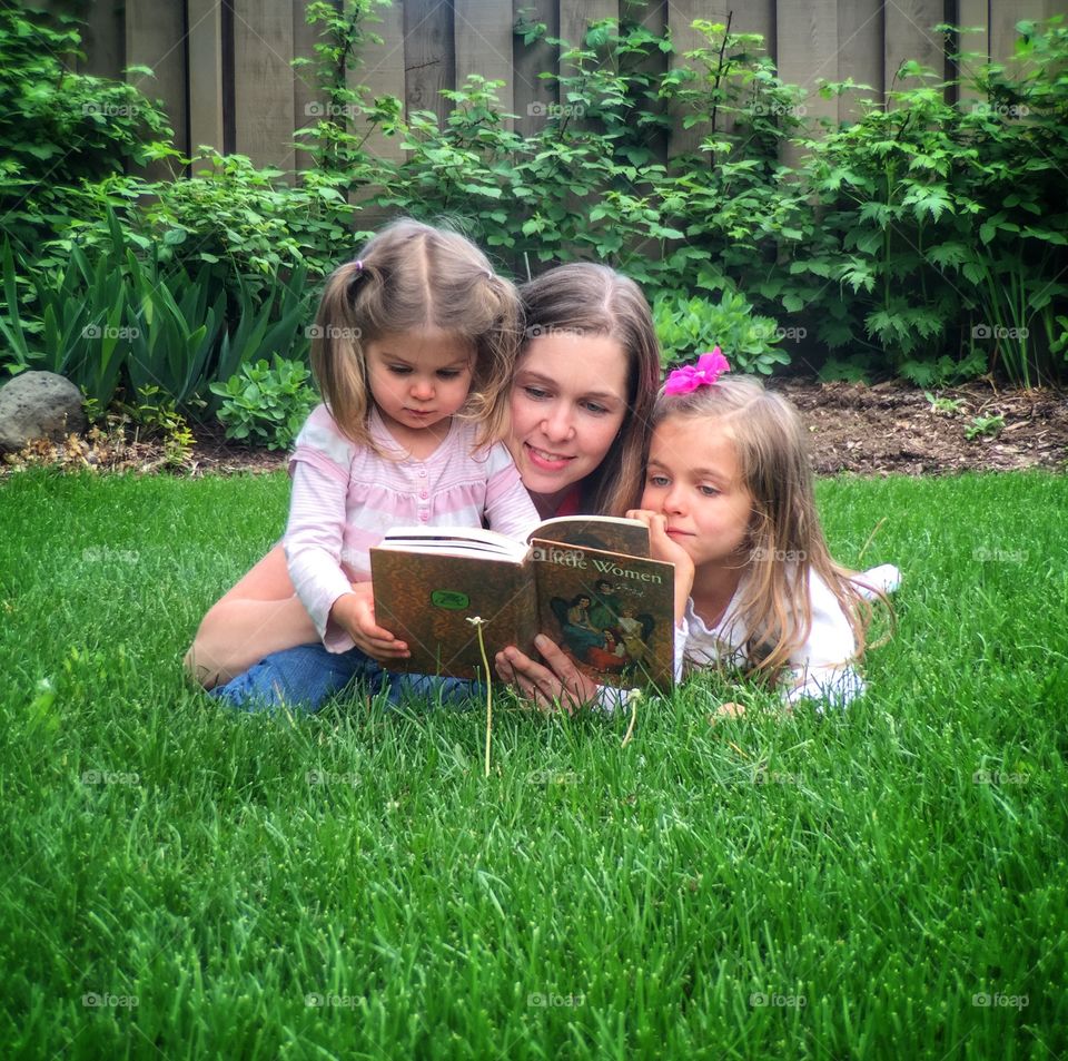 Mother and daughters in park reading story book
