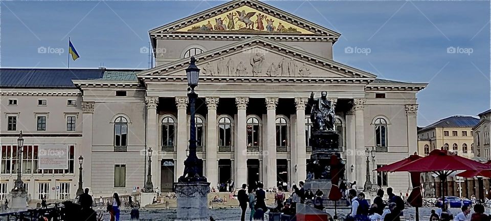 “Max-Joseph Platz” in “Munich” is classically influenced: Ionic columns, triangular rooftops, illustrative reliefs, even inlays of gold. A memorial to king “Max the 1st Joseph” stands in front of the “National Theater”. 2022. Hypnotic Productions