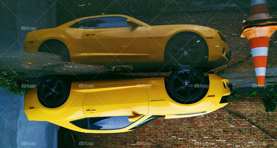 reflection of a yellow chevrolet car in a rain puddle
