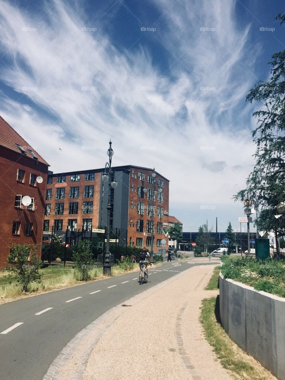Urban park, bike path, colorful buildings in the background, blue sky and green grass on either side 
