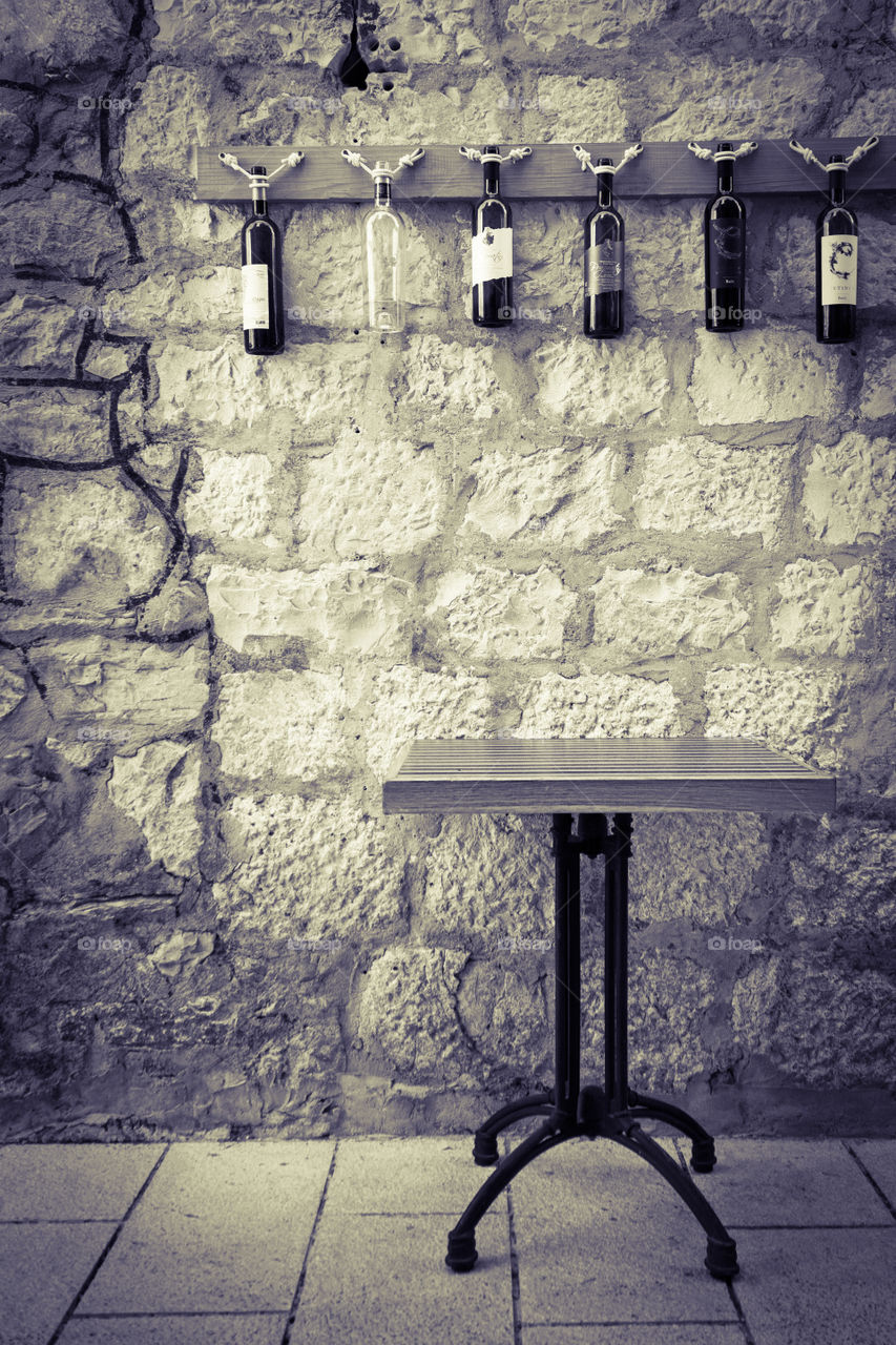 Croatia, Dalmatia, Makarska.  A table near the textured stone wall decorated with glass bottles of wine.  Outdoor cafe