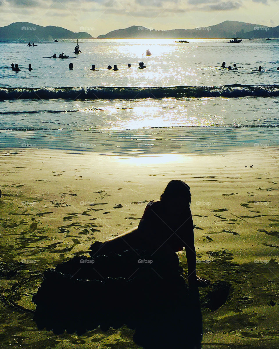 FOAP MISSIONS - The silhouette of the girl playing in the sand with the sun illuminating the Guarujá beach in Brazil. / A silhueta da menina brincando na areia com o sol iluminando a praia do Guarujá, no Brasil. 