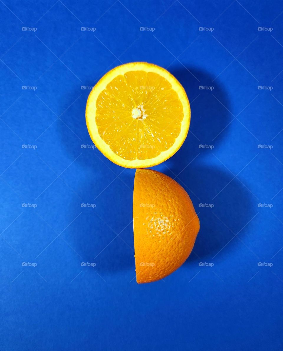 Orange and blue complimentary colours flatlay made on a blue surface with two halves of a fresh orange