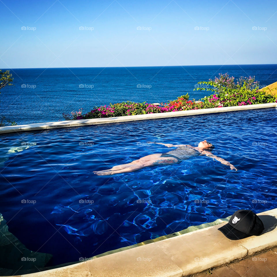 Woman floating in a blue pool with ocean background 