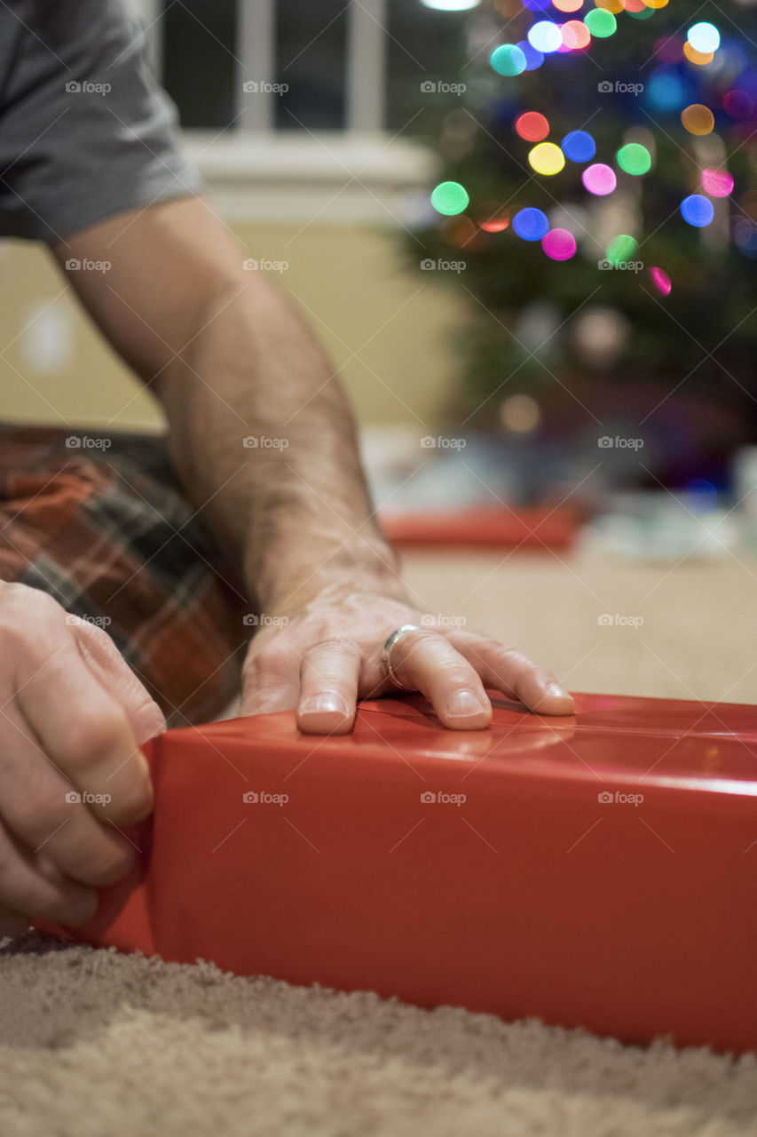 Man wrapping a Christmas present in front of a Christmas Tree 
