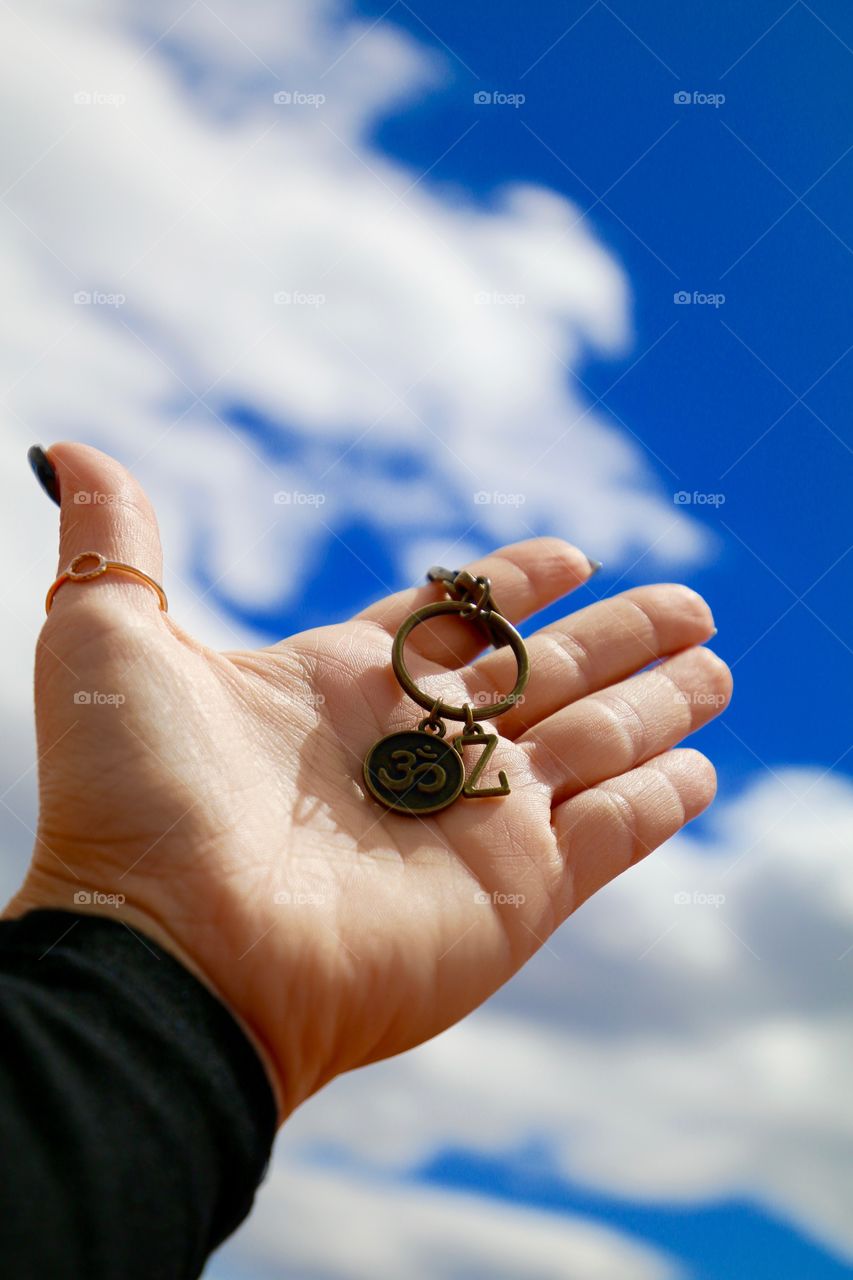 Hand up high holding a keychain with the letter z and the om while looking up at bright blue sky 