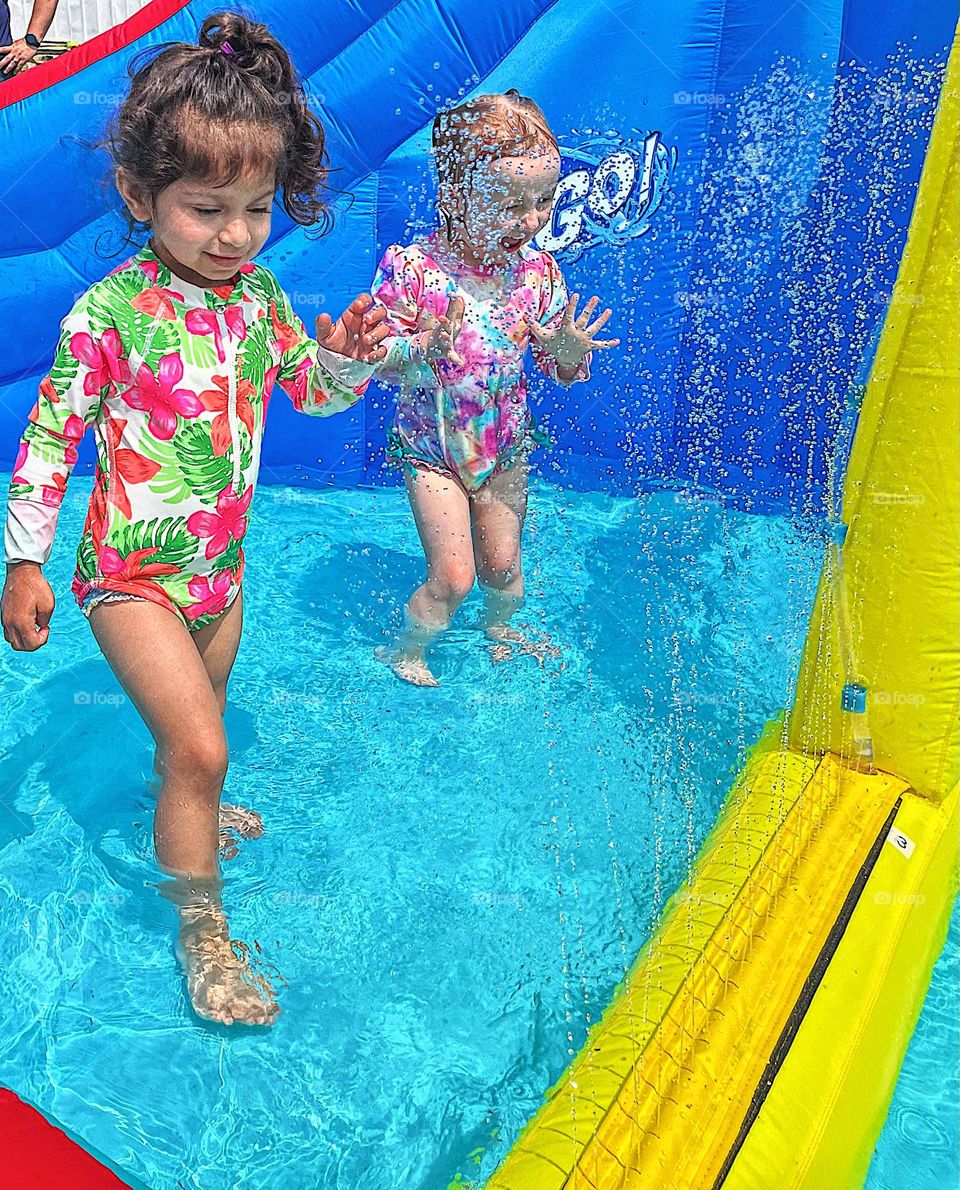 Toddler girls enjoying splash pad and pool, small moments of happiness, splashing in the water in summertime, having fun in the pool, simple fun activities for the summer, toddlers finding happiness outside in the pool