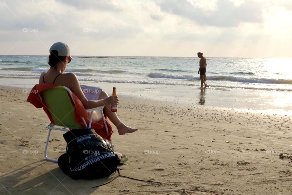 Woman sitting on beach chair with bottle of beer enjoy sunset