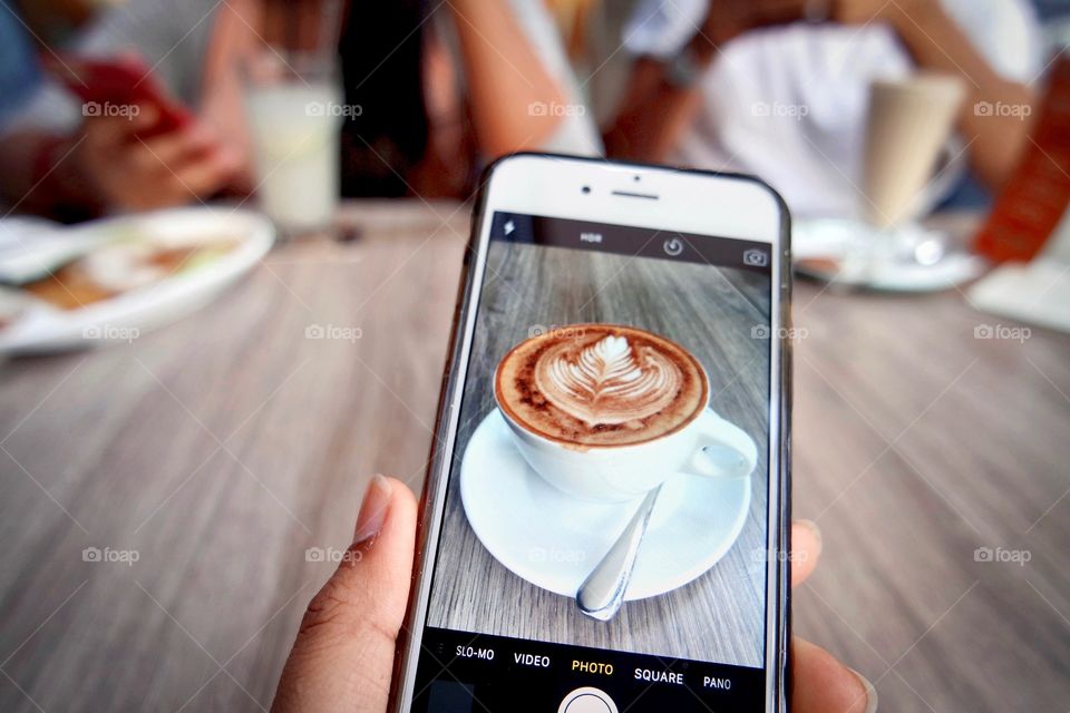 Human hand taking photograph of coffee with mobile phone