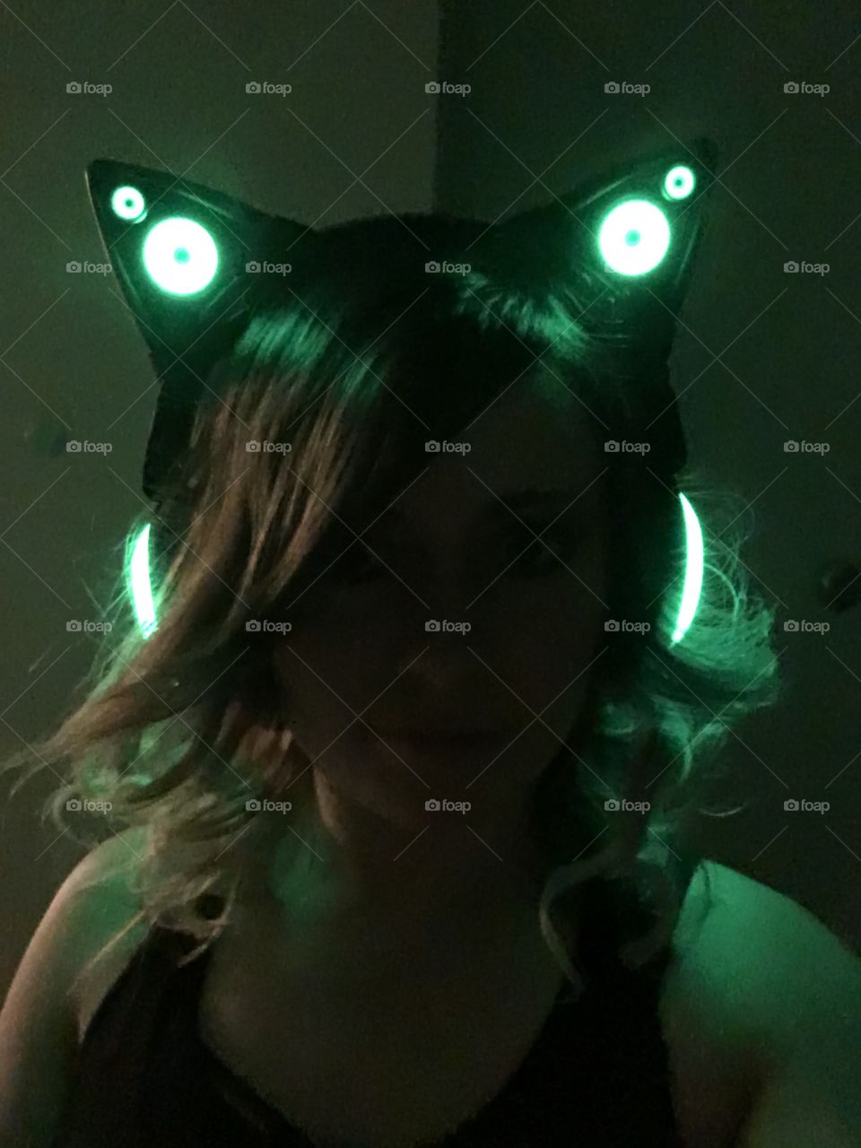 Glowing green cat ear headphones on in a dark room